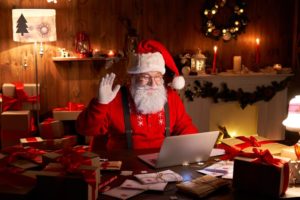 Santa sitting at his desk waving at a computer camera